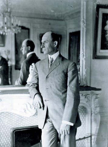 Wilbur Wright standing, facing to his right, with his elbow on a fireplace mantel in Hart O. Berg's Paris apartment.