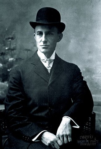 Head and shoulders studio portrait of Wilbur Wright seated in a chair wearing a dark suit and a bowler hat.