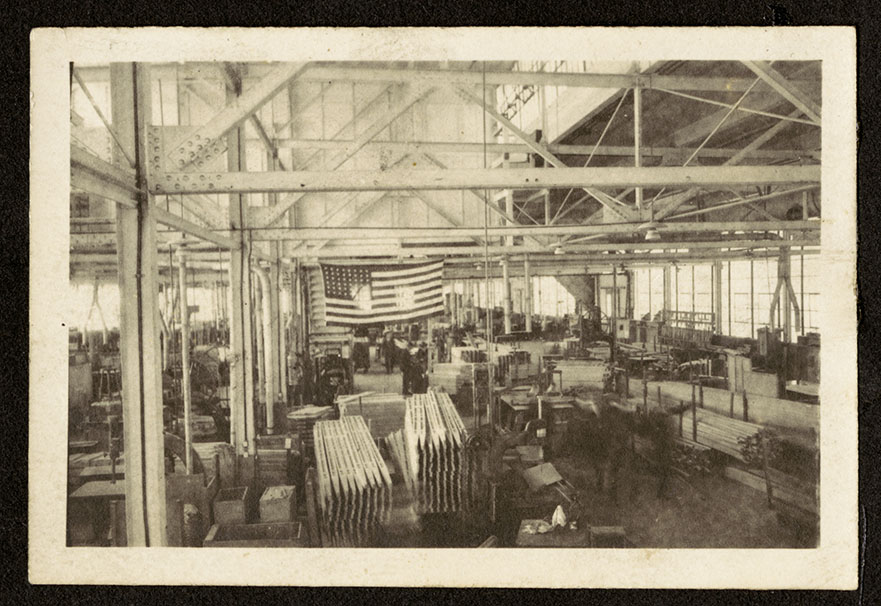 An interior view of the Dayton-Wright Airplane Company, Plant 1, Mill department (wood shop), which was supervised by Wilbur Bigelow. A large American flag can be seen hanging from the beams, and various wooden components are on cart. Circa 1917-1919. (sc347_05_21)